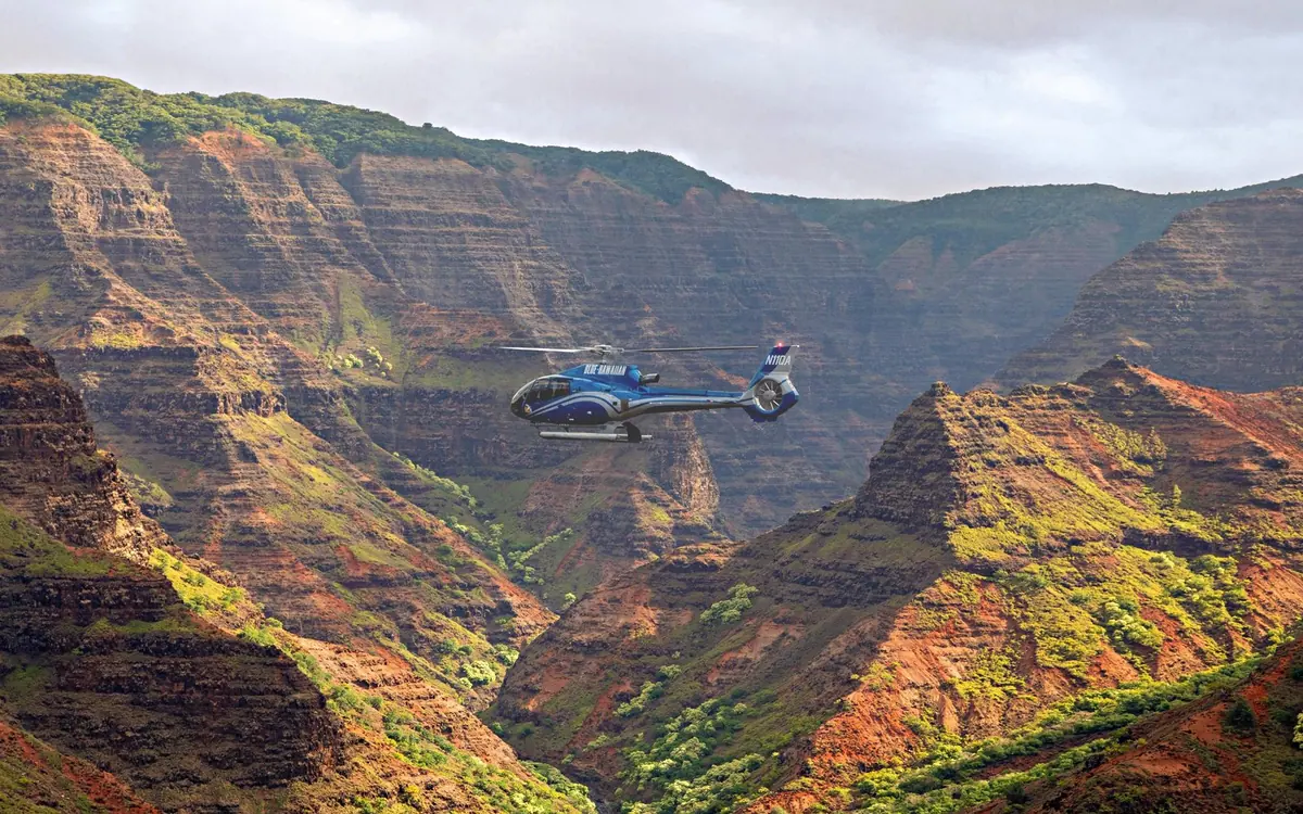 A helicopter flying above the red walls of Waimea Canyon