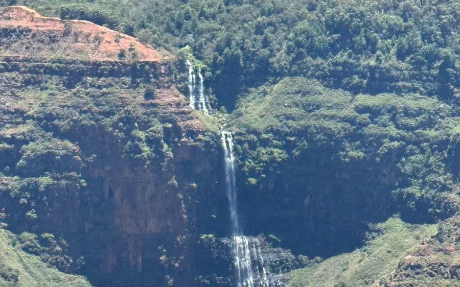 A thin waterfall falling down a green cliff inside the canyon