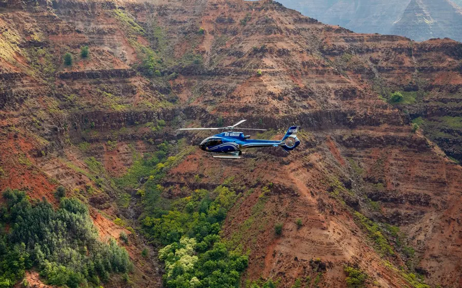 A blue helicopter above the red ridges of the canyon on Kauai