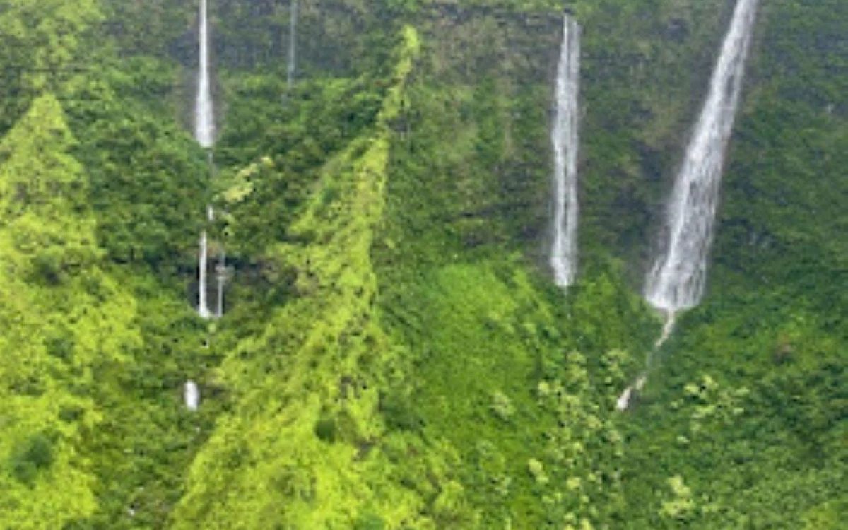 Thin waterfalls dropping down green cliffs, photographed from the air